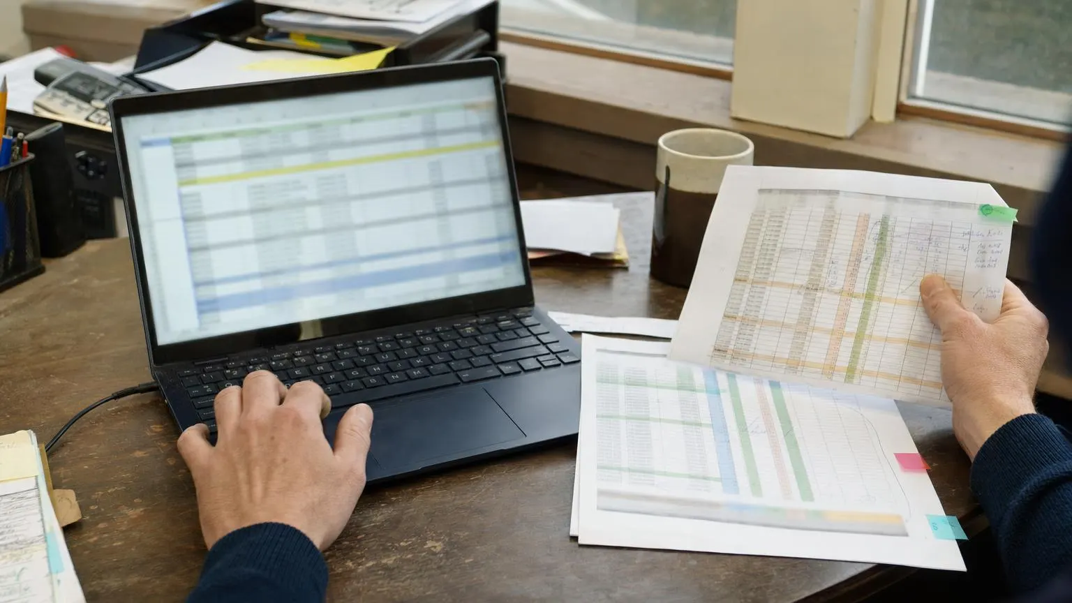 Laptop met onleesbaar rekenblad naast verschillende afgedrukte Excelversies op kantoor